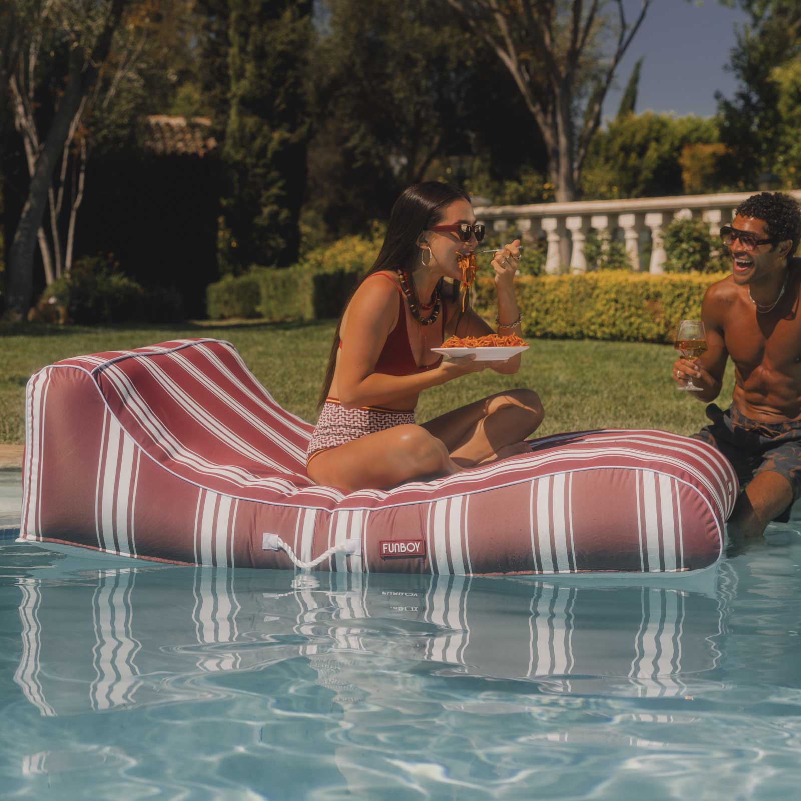 Two people enjoying a poolside moment with a striped inflatable lounger.