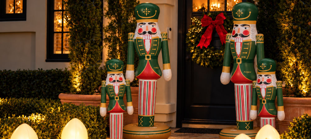 Four Christmas nutcracker yard decorations in green, red, and white striped uniforms, displayed on a front porch with holiday wreaths and warm string lights.