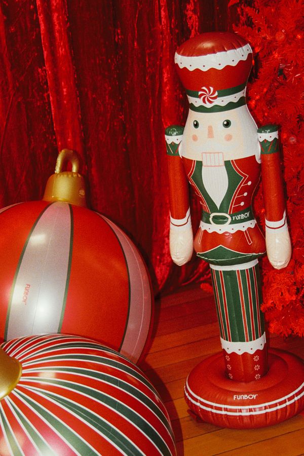 A festive red, green, and white inflatable nutcracker figure standing next to large striped red, white, and green holiday ornaments against a red sequined backdrop.