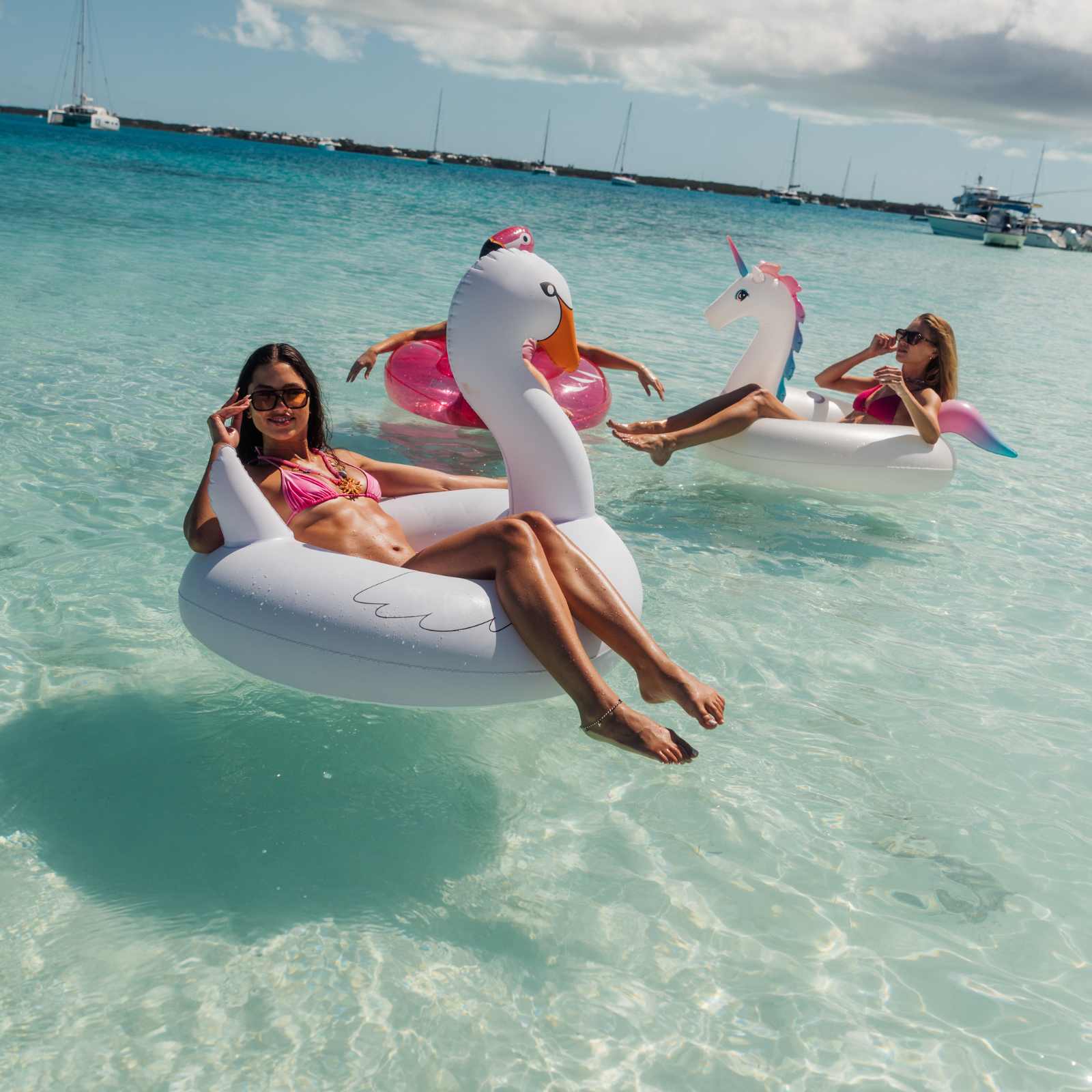 People floating on inflatable swan and unicorn pool floats in clear water with boats in the background.
