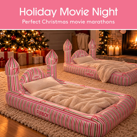 Two inflatable castle-shaped pet beds with pink and green striped walls and cream faux-fur bedding, shown in a cozy holiday living room with a Christmas tree, fireplace, and wrapped gifts. A pink banner at the top reads 'Holiday Movie Night' and 'Perfect Christmas movie marathons.