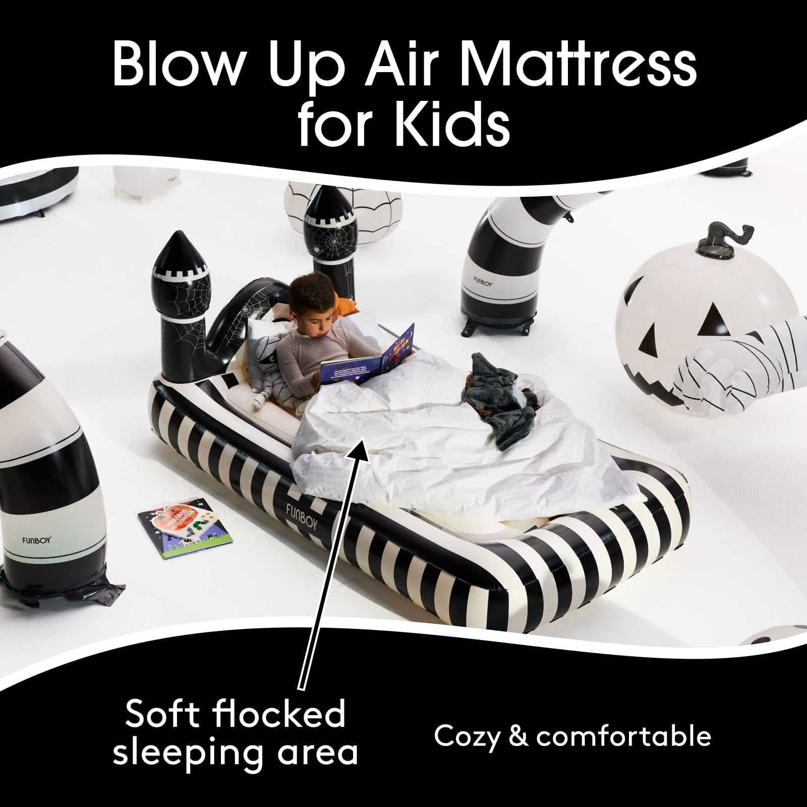 An inflatable kids' sleeping mat with a black and white striped design, featuring a child sitting inside reading a book. The scene is decorated with Halloween-themed inflatable props like a jack-o'-lantern and a zombie, on a white background with promotional text overlays.