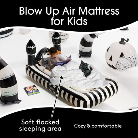 An inflatable kids' sleeping mat with a black and white striped design, featuring a child sitting inside reading a book. The scene is decorated with Halloween-themed inflatable props like a jack-o'-lantern and a zombie, on a white background with promotional text overlays.
