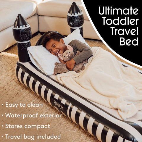 A child lying on an inflatable castle-shaped travel bed in a living room setting, with a black and white castle design, white pillows, and a cream blanket. Text overlays describe the product features and branding.