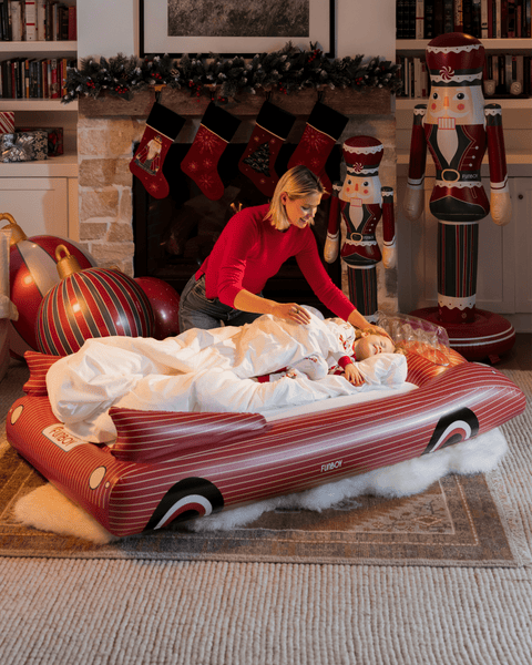 Woman with child on a red inflatable car in a festive living room with Christmas stockings and decorations.