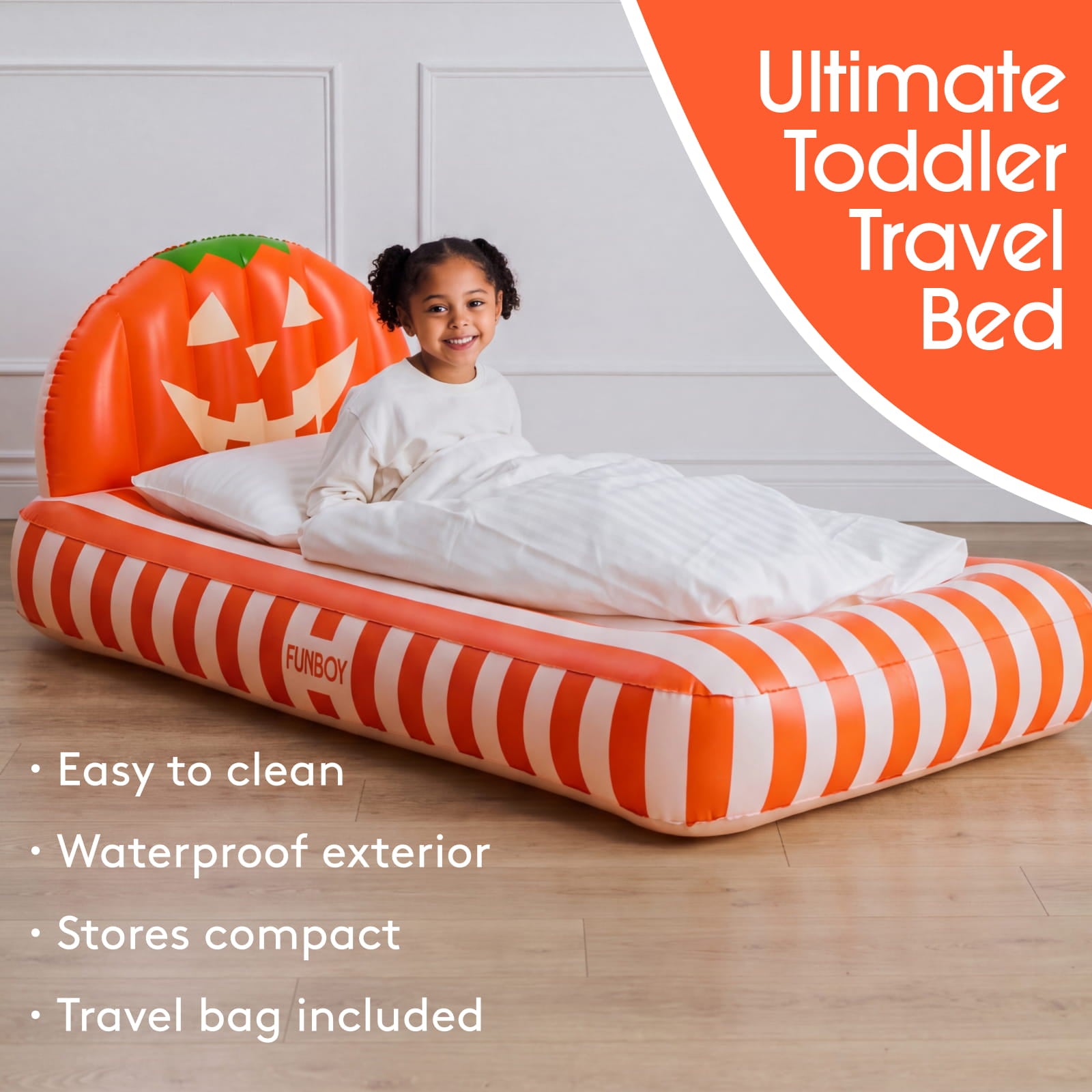 An inflatable toddler travel bed with a pumpkin-shaped headboard, shown with a young child sitting on it in a bedroom setting. The bed has orange and white stripes on the sides and a green pumpkin design on the backrest.