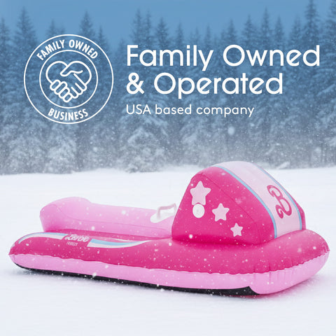 A pink inflatable snowmobile slide toy placed in a snowy outdoor scene with pine trees in the background. White text at the top reads 'Family Owned & Operated' and 'USA based company,' with a circular 'Family Owned Business' logo on the left.