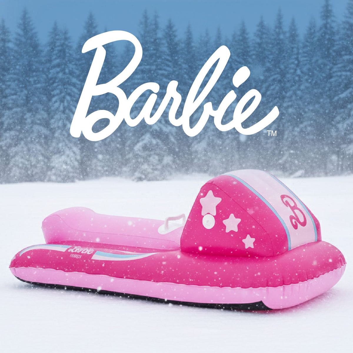 A pink Barbie-branded inflatable float or sled-like toy shown outdoors in the snow, with a blurred winter forest background and large white Barbie logo text across the top.