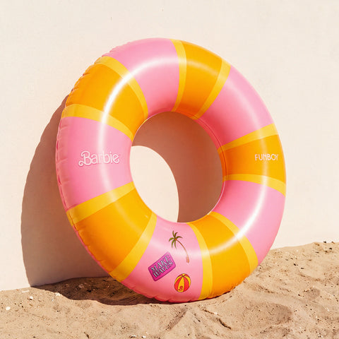 Pink and yellow inflatable ring with 'Barbie' branding on a sandy background