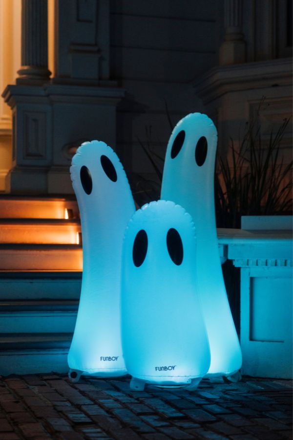 Three ghost-shaped outdoor inflatable lamps glowing with a cool blue light, featuring black oval eyes and the brand name 'TURBO' near the base, set on a brick patio in front of a building at night.