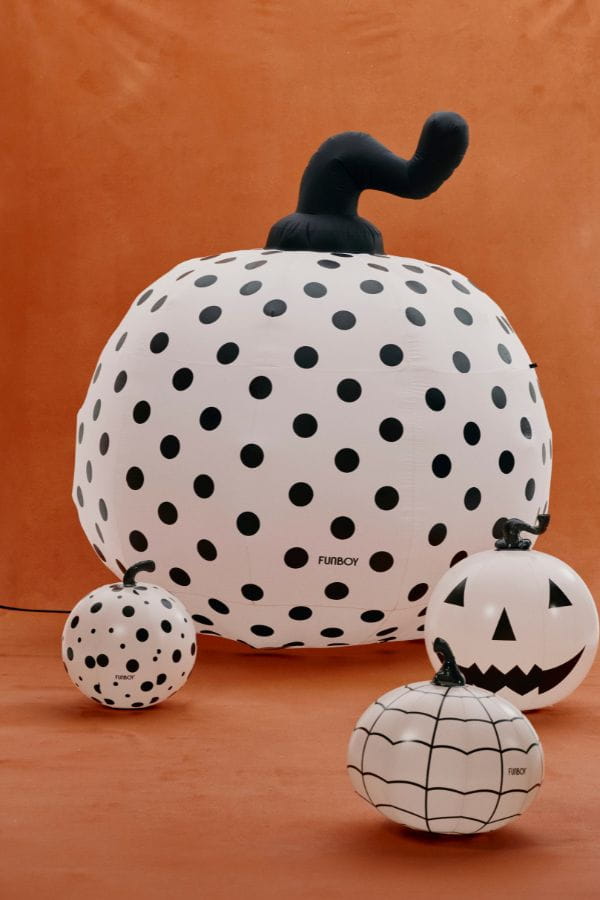 A Halloween decoration set featuring three inflatable jack-o'-lantern pumpkins with black and white designs, including polka dots, spiderweb patterns, and a carved face, displayed against a solid orange background.