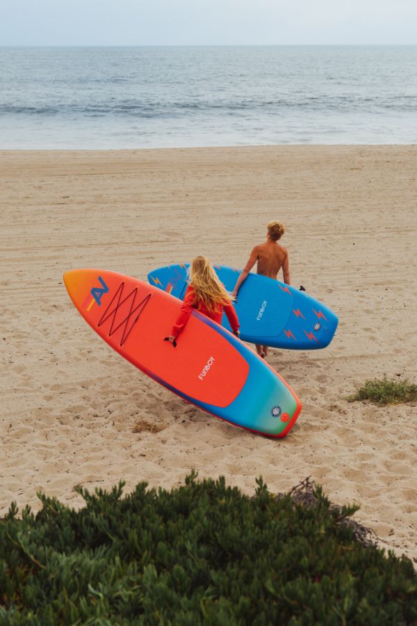 Two people carrying colorful surfboards on a beach