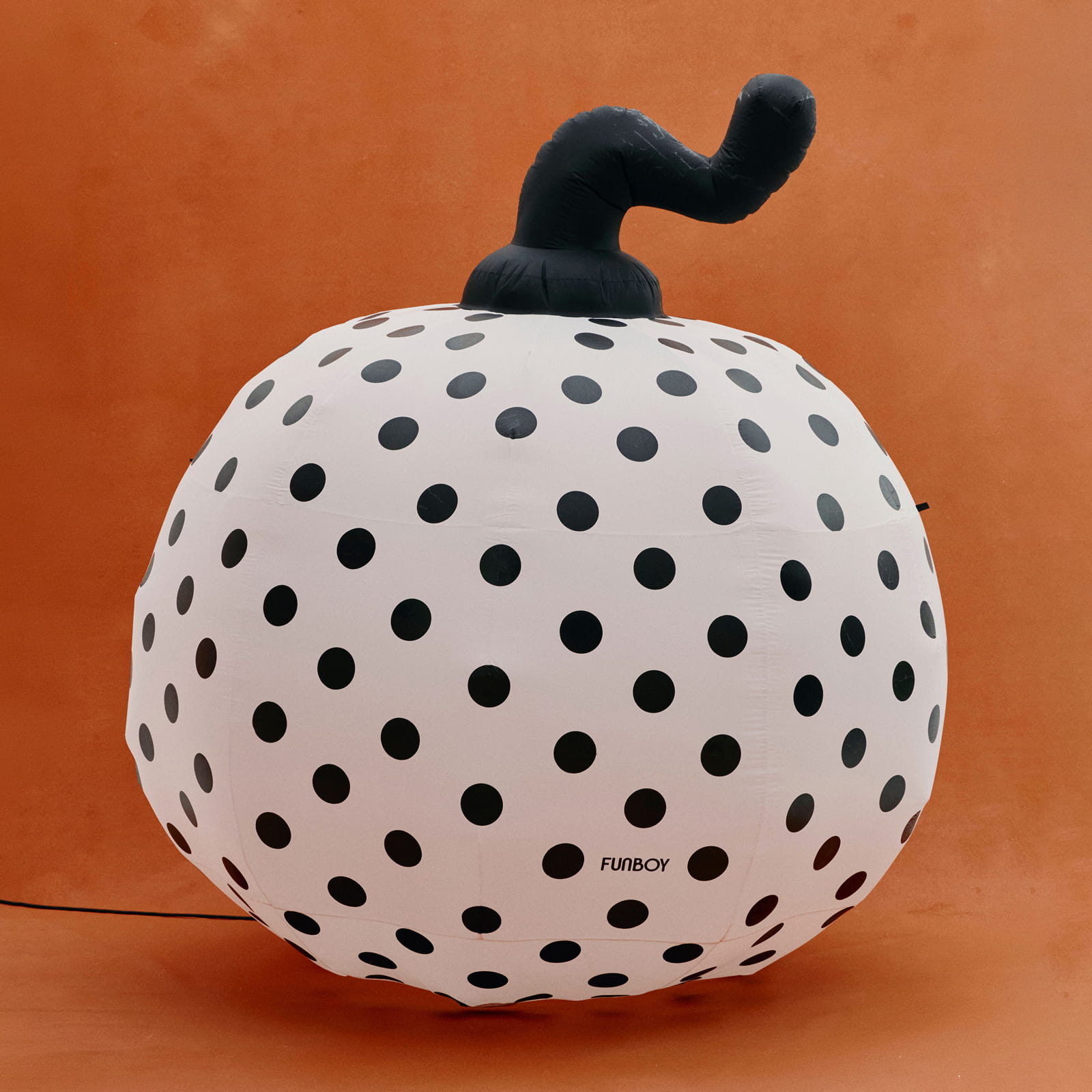 An inflatable pumpkin-shaped light with a white body covered in black polka dots and a black stem, photographed against a solid orange background. The brand name 'FUNBOY' is printed near the bottom right of the pumpkin.