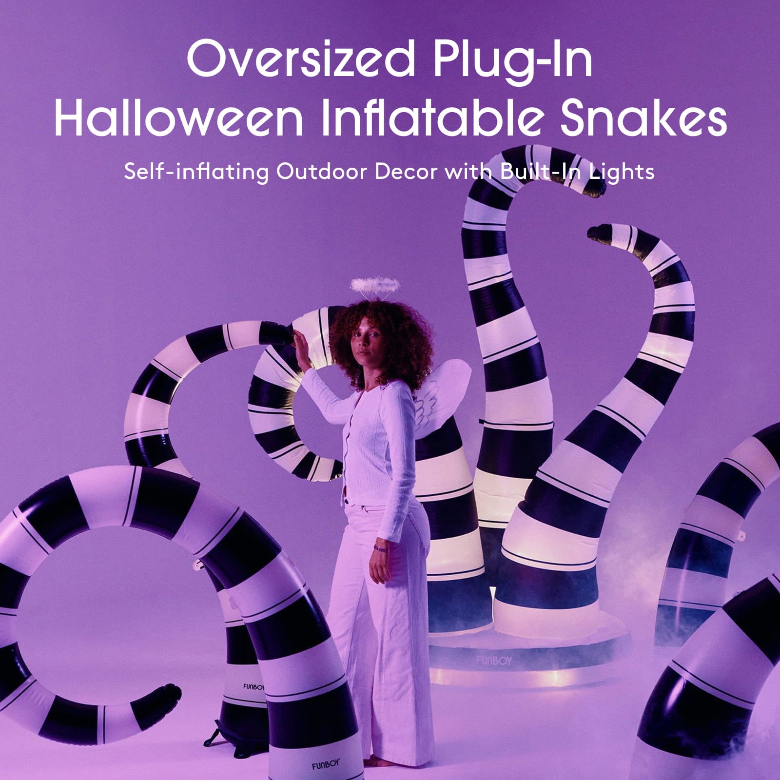 A person stands in a studio wearing a white outfit and posing with oversized inflatable snakes that are glowing with black-and-white stripes. Large text at the top reads 'Oversized Plug-In Halloween Inflatable Snakes' and 'Self-inflating Outdoor Decor with Built-In Lights.