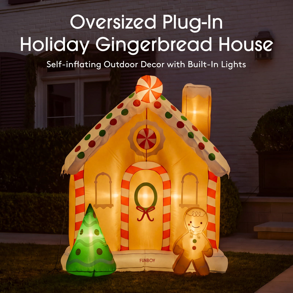 An oversized inflatable gingerbread house holiday outdoor decor decoration shown lit up at night in front of a house. The house features red and white striped details, a green wreath on the door, a small green Christmas tree, and a gingerbread man figure.