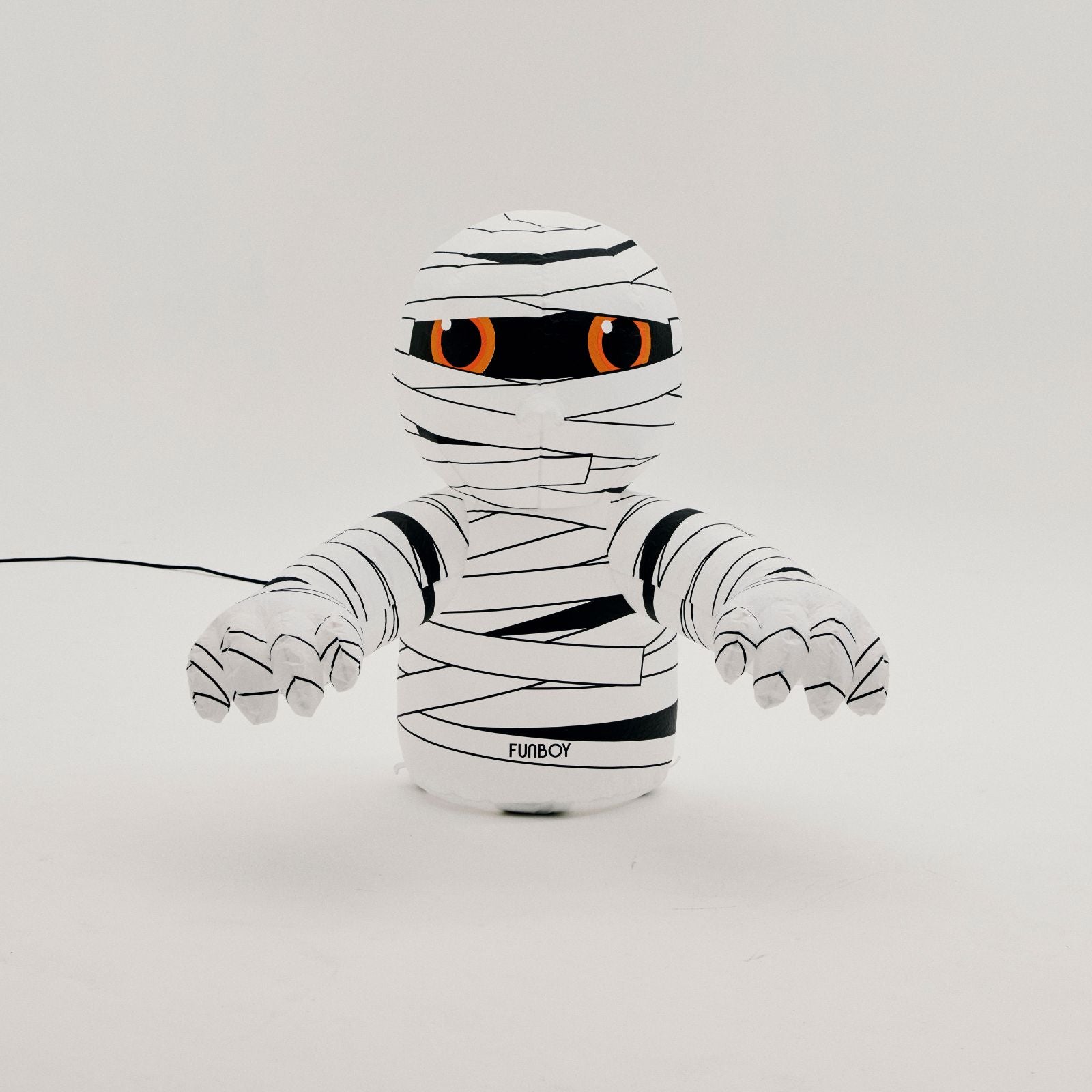 A white and black mummy-themed toy or plush figure with orange eyes, shown against a plain light gray background. A black power cord extends from the left side, and the brand name 'FLYBECH' is printed near the base.