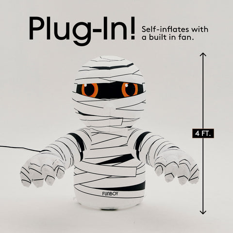 Inflatable mummy toy with orange eyes, wrapped in black and white bandages, shown with text overlays 'Plug-In! Self-inflates with a built in fan.' and a '4 FT.