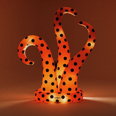 An inflatable octopus halloween snake decoration with glowing orange and black polka dots, standing on a matching circular base against a warm brown background.