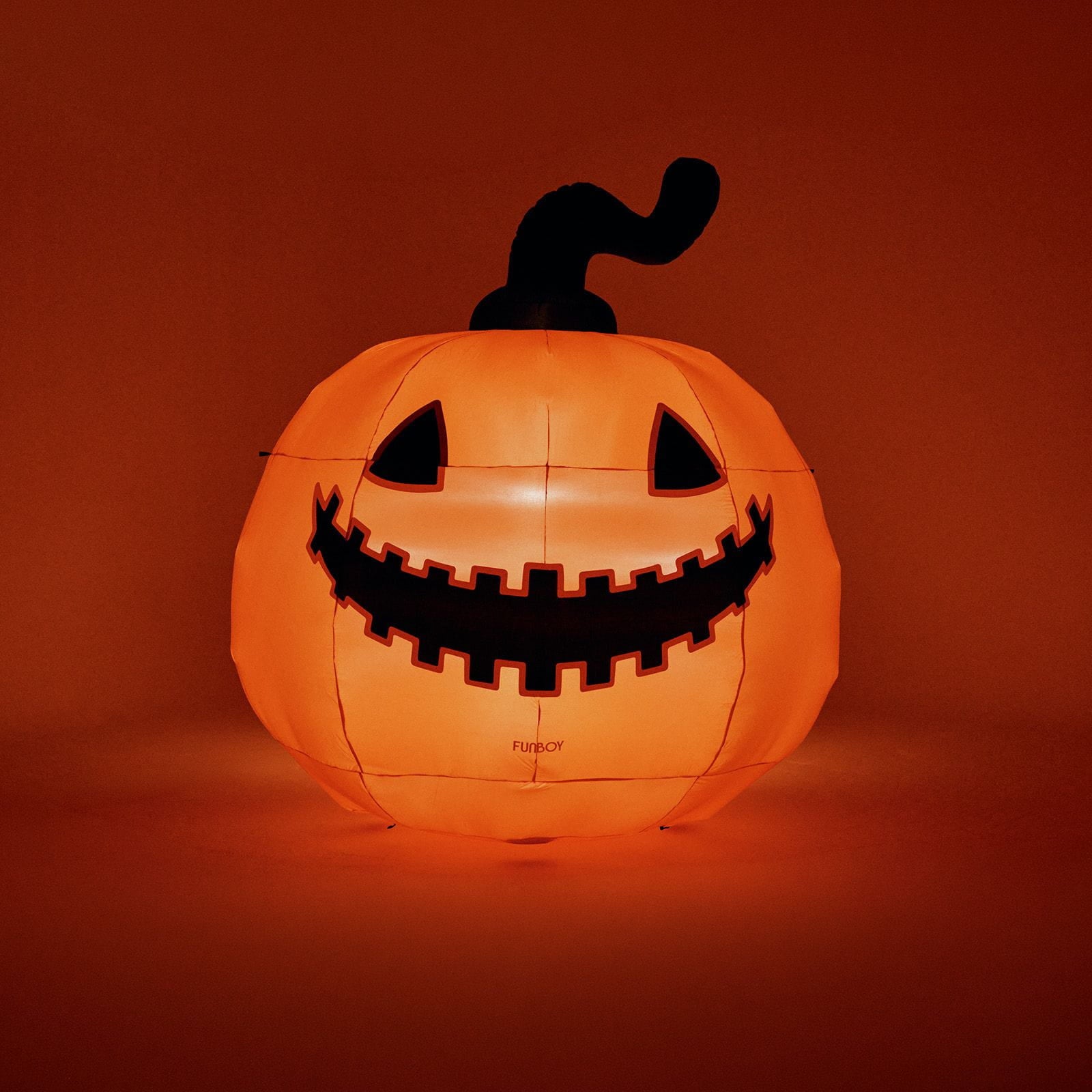 An inflatable glowing jack-o'-lantern pumpkin with a carved black face and stem, illuminated from within against a dark orange background.