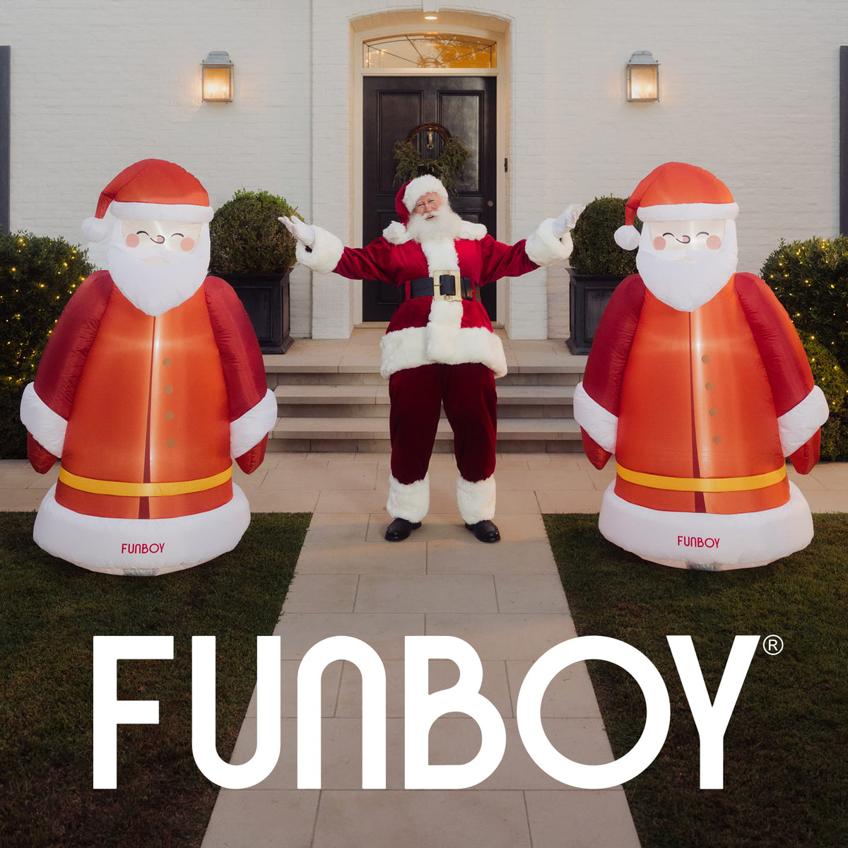 A person in a Santa Claus costume stands between two large inflatable Santa Claus figures on a front lawn, with a house entrance behind them. The words FUNBOY appear prominently at the bottom of the image.