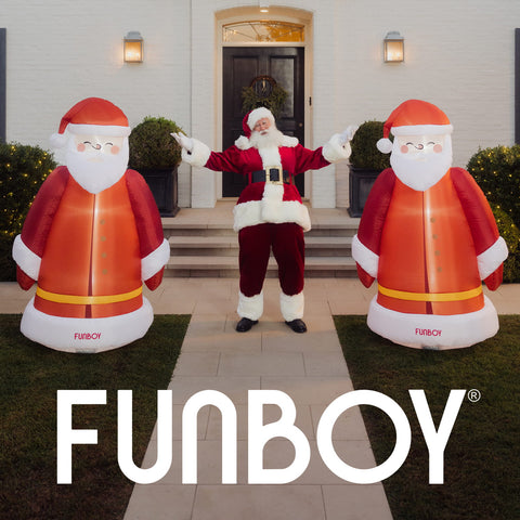 A person in a Santa Claus costume stands between two large inflatable Santa Claus figures on a front lawn, with a house entrance behind them. The words FUNBOY appear prominently at the bottom of the image.