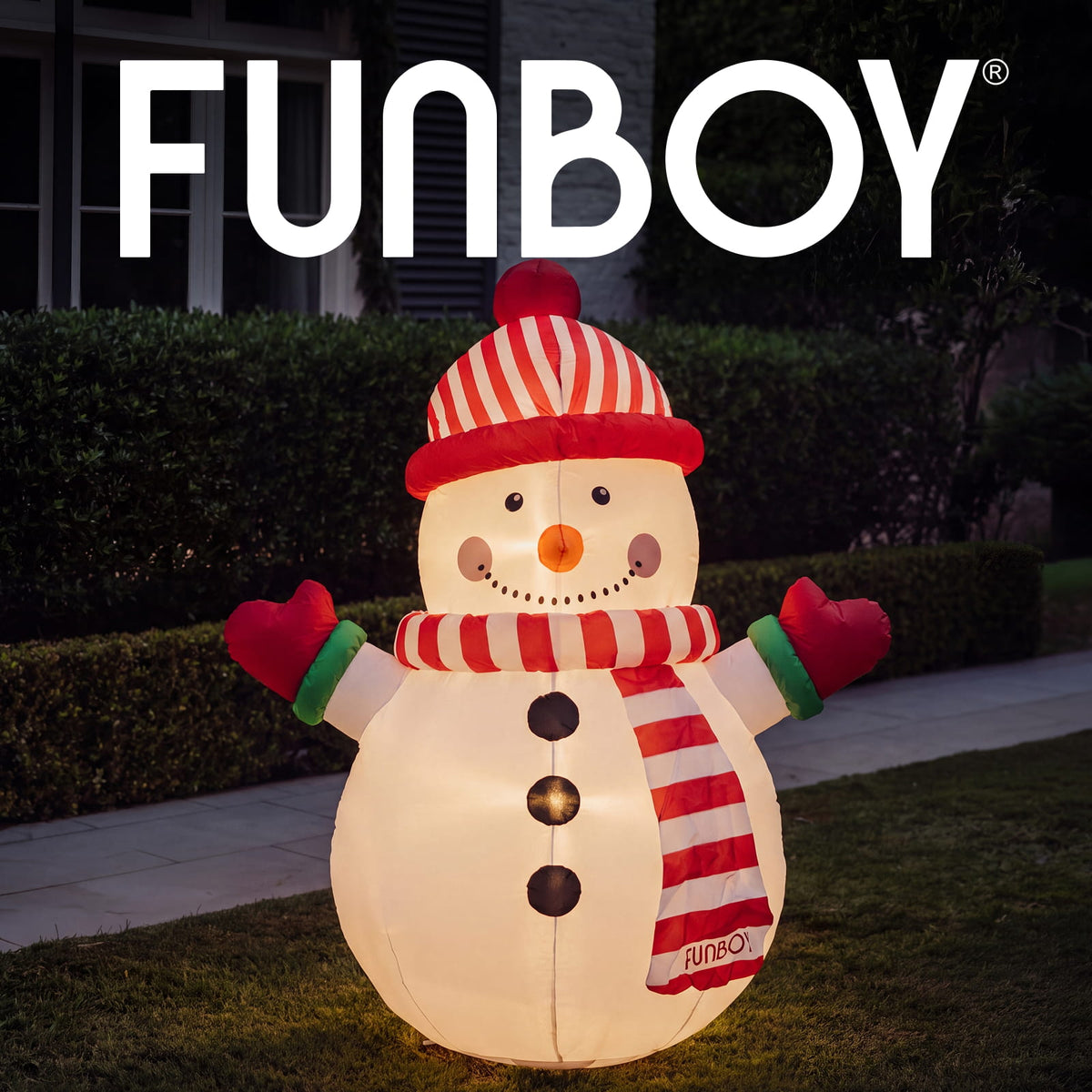 A large inflatable snowman decoration standing on a lawn in front of a house at night. The snowman is glowing with warm white light and wears a red-and-white striped hat, matching scarf, red mittens, and black buttons.