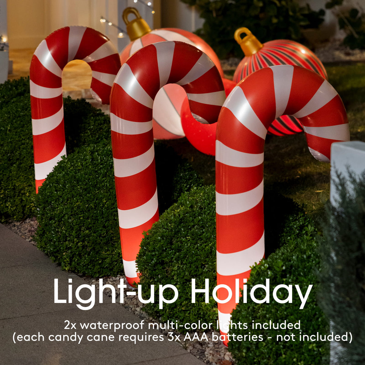 Two large inflatable candy cane yard lights with red and white stripes, shown lit at night in a landscaped garden setting. Text overlay reads 'Light-up Holiday' with battery information.