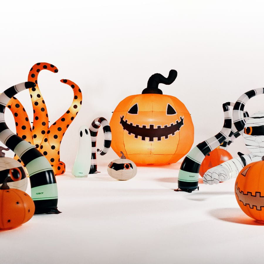 A collection of inflatable Halloween decorations arranged on a white studio floor, including a large jack-o'-lantern, striped spiderwebs, mummies, ghost figures, and smaller pumpkins.