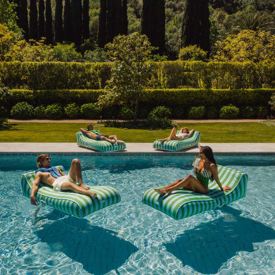 People relaxing on striped inflatable pool floats in a pool surrounded by greenery.