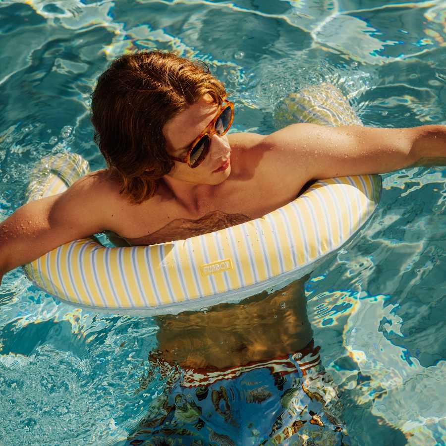 Man in sunglasses and swim trunks with a striped inner tube in a pool