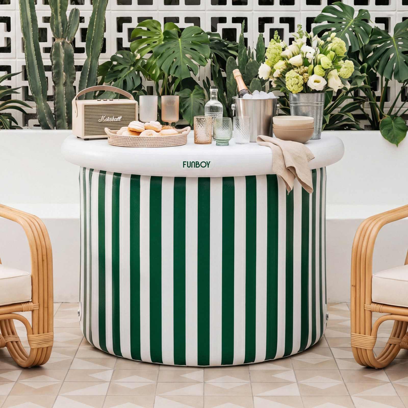 Green and white striped inflatable bar with drinks and snacks on a patio with plants and chairs.