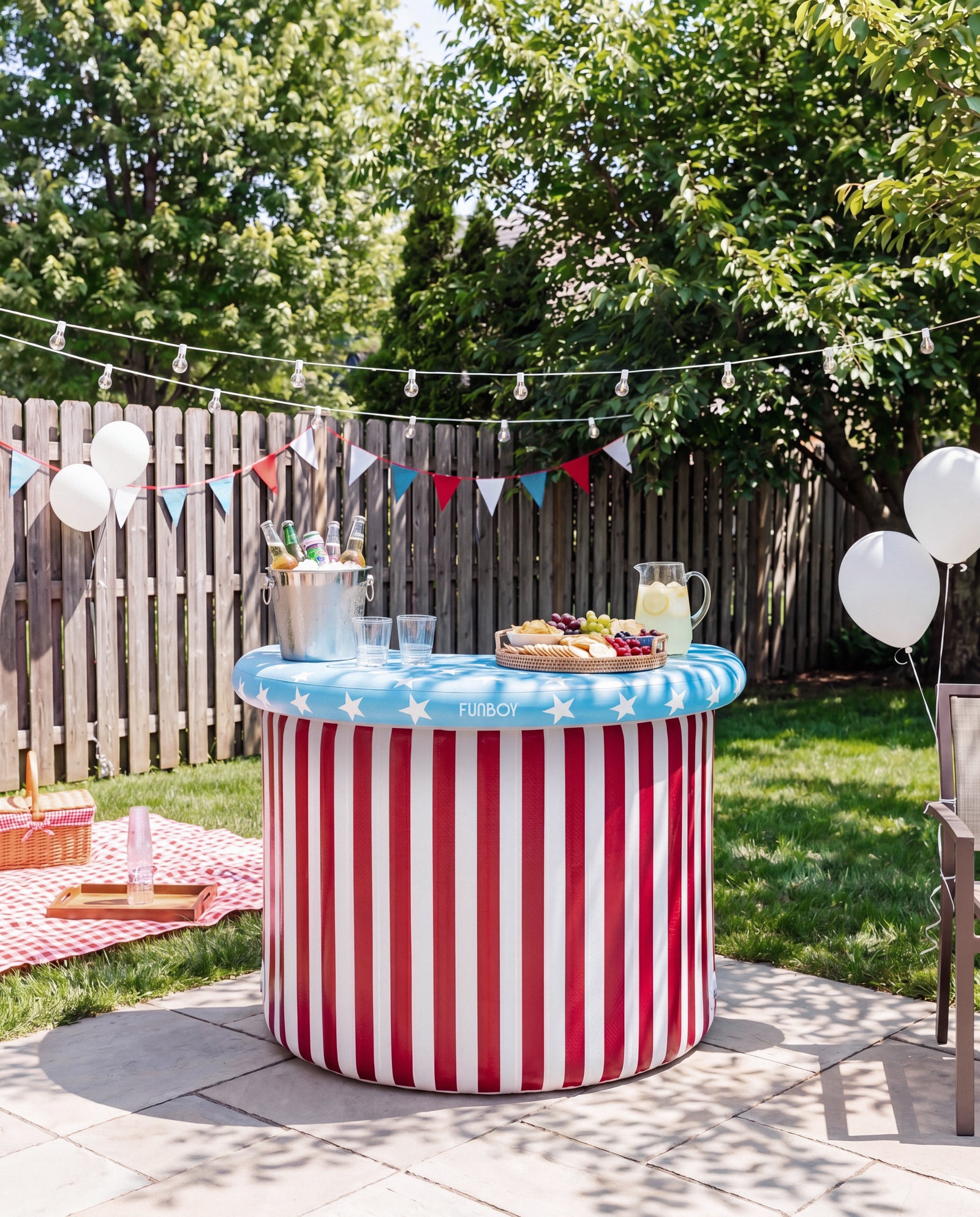 Red, white and blue 4th of July inflatable party bar. Outdoor setting with a red and white striped table, drinks, and snacks on a sunny day.