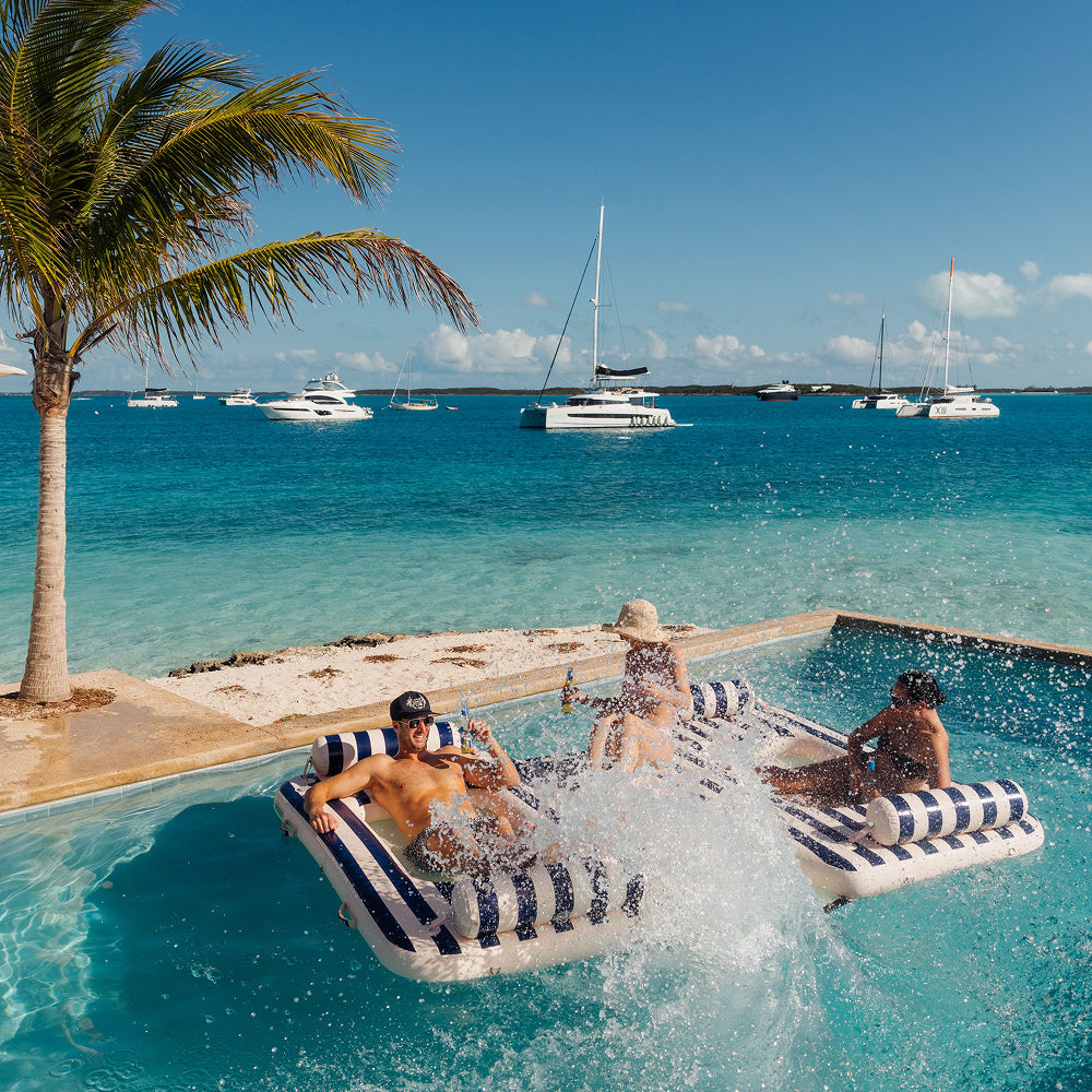 People enjoying a pool party on a sunny day with boats in the background. The float is a  striped inflatable navy and white striped party island by FUNBOY.