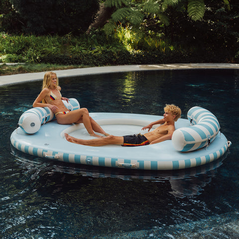 Two people relaxing on a circular inflatable pool float in a pool.