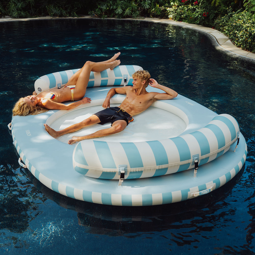 Two people lying on a striped inflatable pool float in a pool.