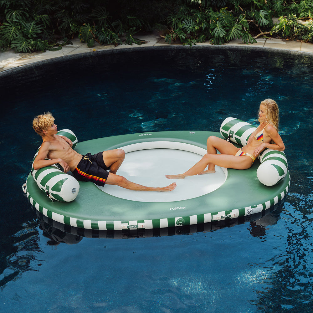 Two people relaxing on a green and white striped pool float in a pool.