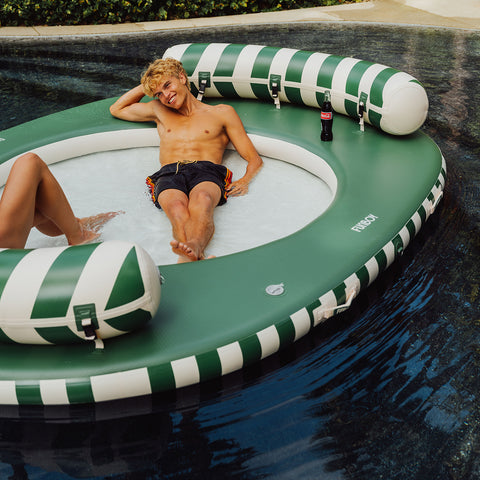 Two people lounging on a green and white striped inflatable pool toy in a pool.