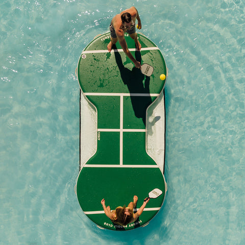 Two people playing paddle ball on a large green paddle ball court in a pool. FUNBOY Paddle Club