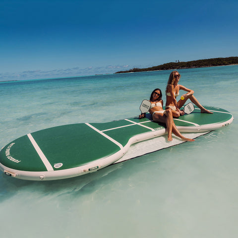Two people sitting on a large green and white inflatable paddleboard in clear blue water.