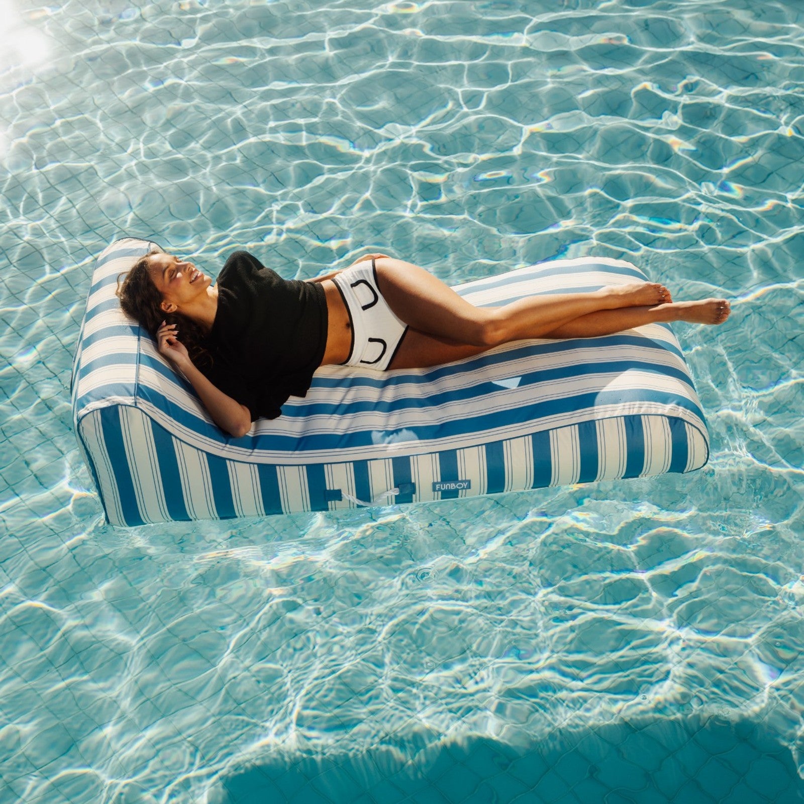 Person lying on a striped fabric blue pool float in clear blue water