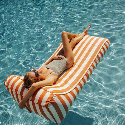 Woman relaxing on a orange and white striped pool float in clear blue water