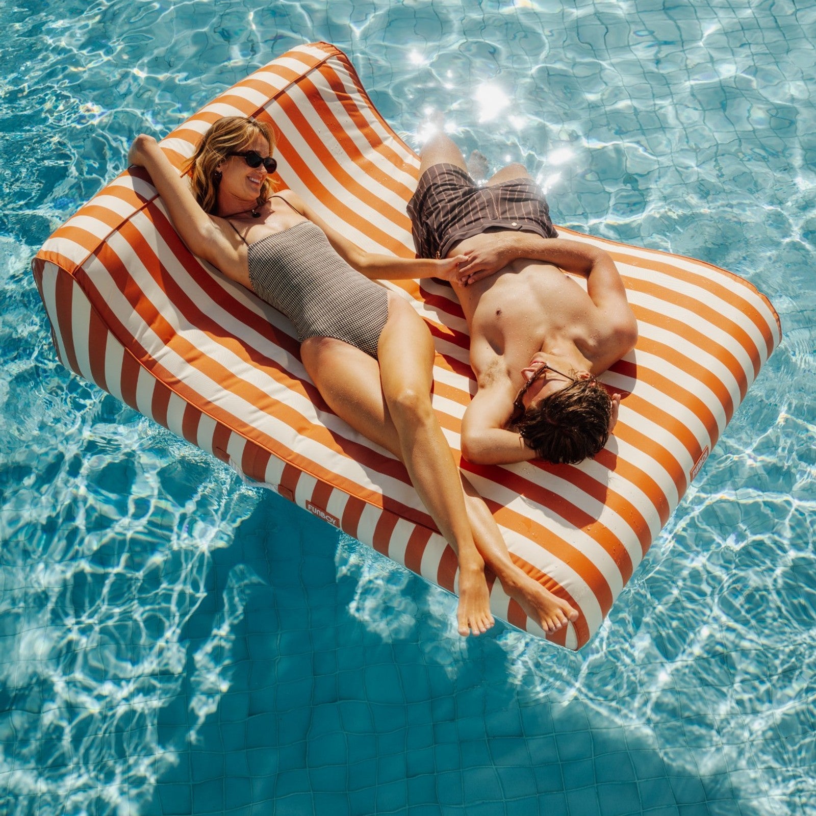 Two people lying on a striped inflatable raft in a pool