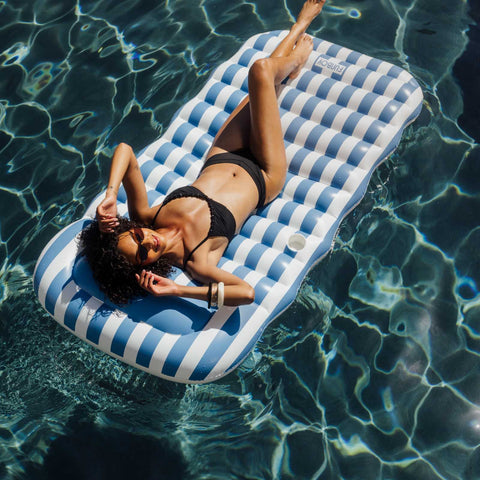 Woman relaxing on a blue and white striped inflatable pool float in clear water.