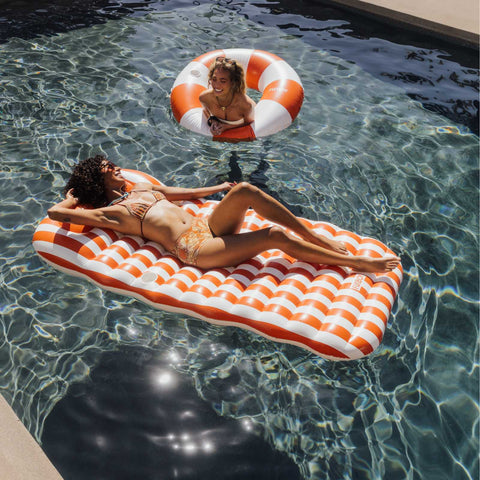 Two women enjoying a sunny day in a pool with orange and white striped floaties.