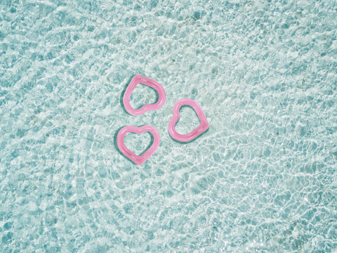 Three pink heart-shaped inflatable pool floats on a textured blue surface