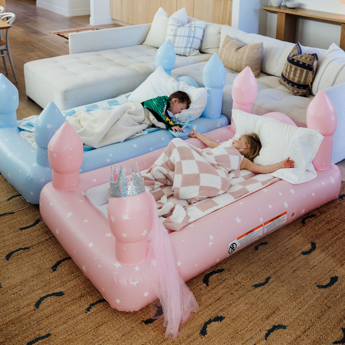 Children sleeping on FUNBOY inflatable princess and castle sleepover beds in living room.