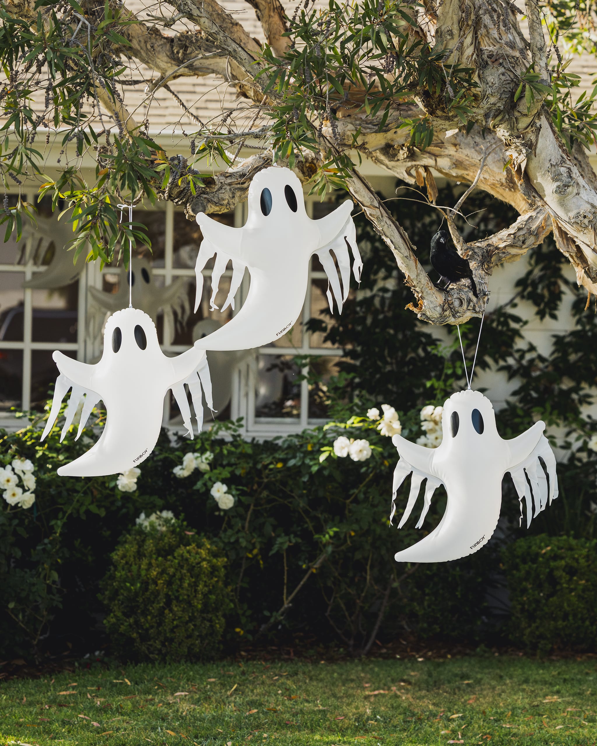 Hanging ghost decorations on a tree branch with a house and garden in the background