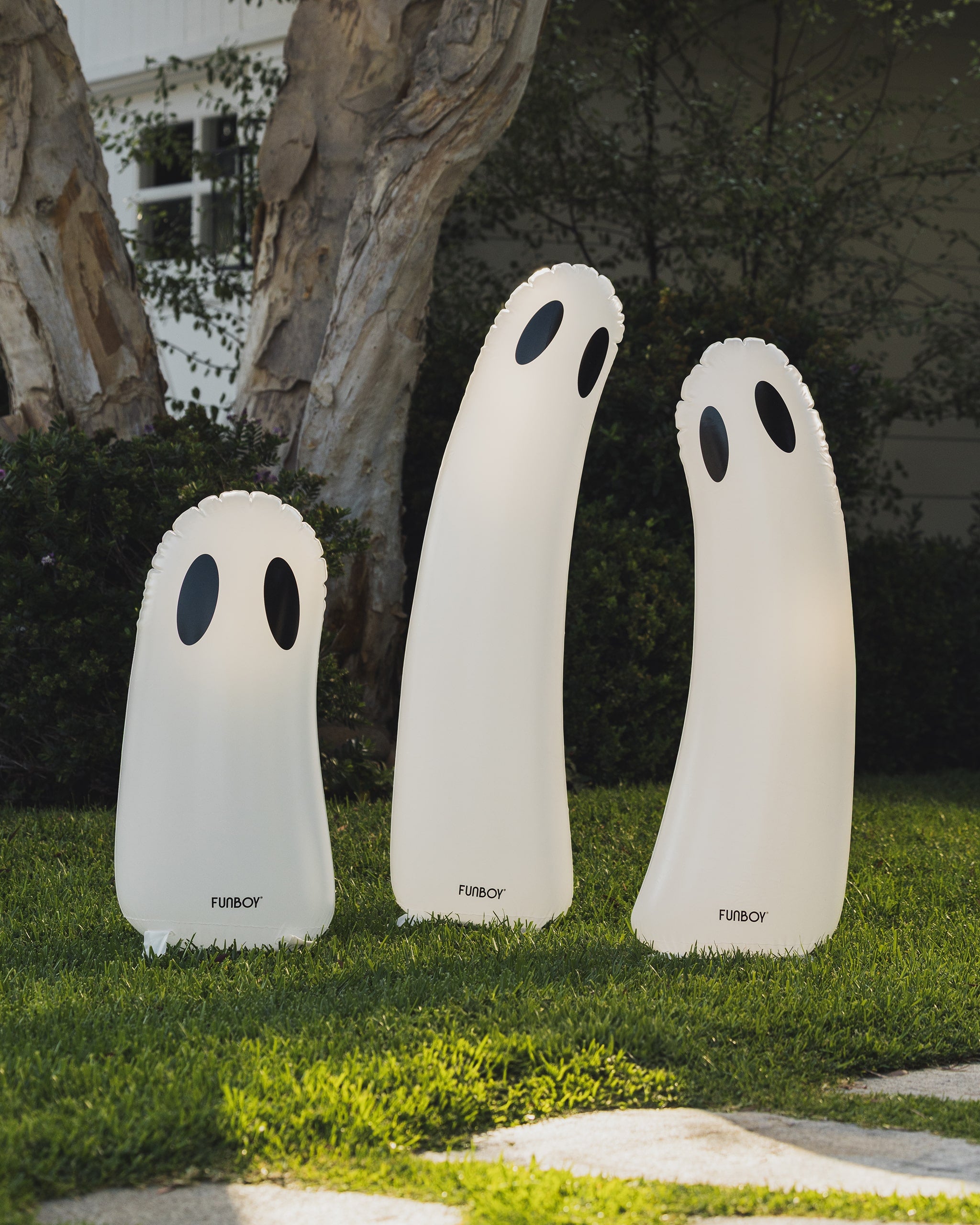 Three illuminated ghost-shaped outdoor lights on a grassy lawn