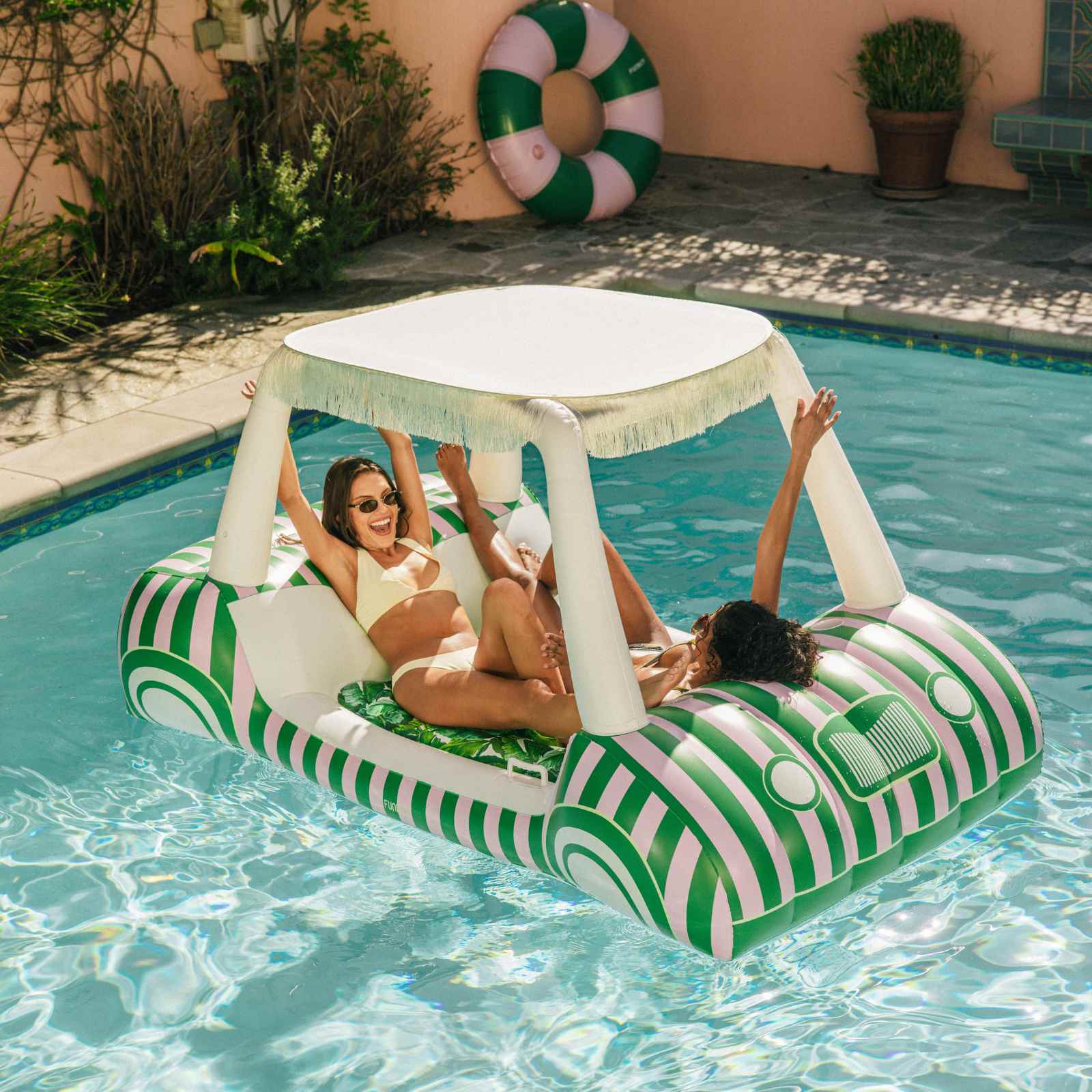 Three people on a green and white striped golf cart pool float in a pool.