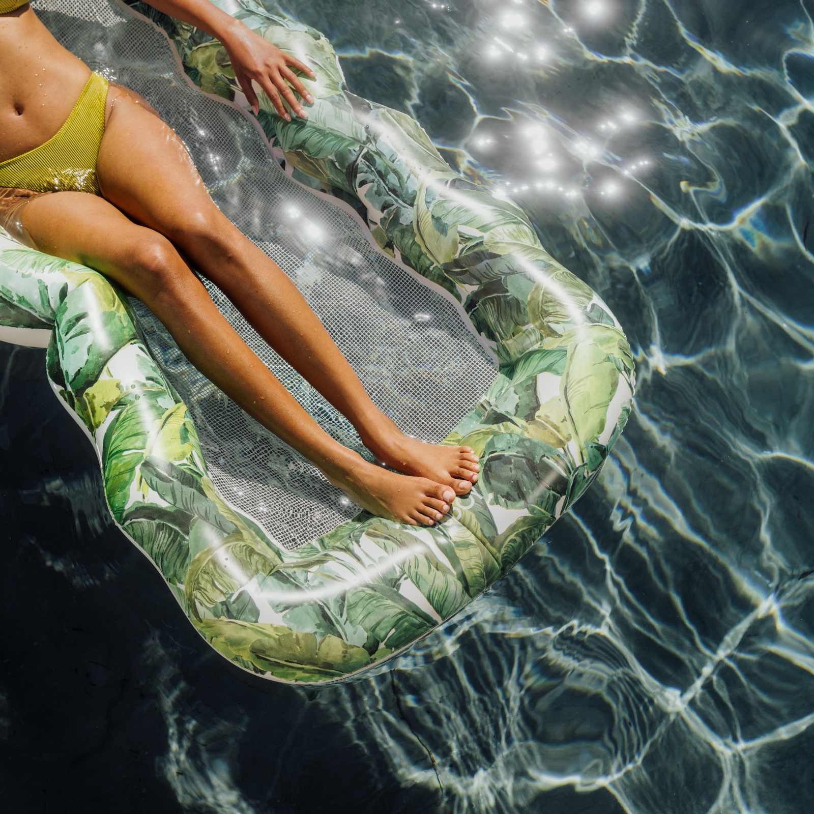 Person lounging on a leaf-patterned inflatable pool float in clear water.